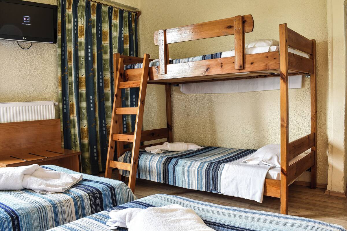 A room with bunk beds, a wooden ladder, a TV, and a window with curtains.
