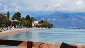 A coastal view with a beach, a mountain in the background, and a chair with a drink. - Kanelli Beach (Aigialeia)