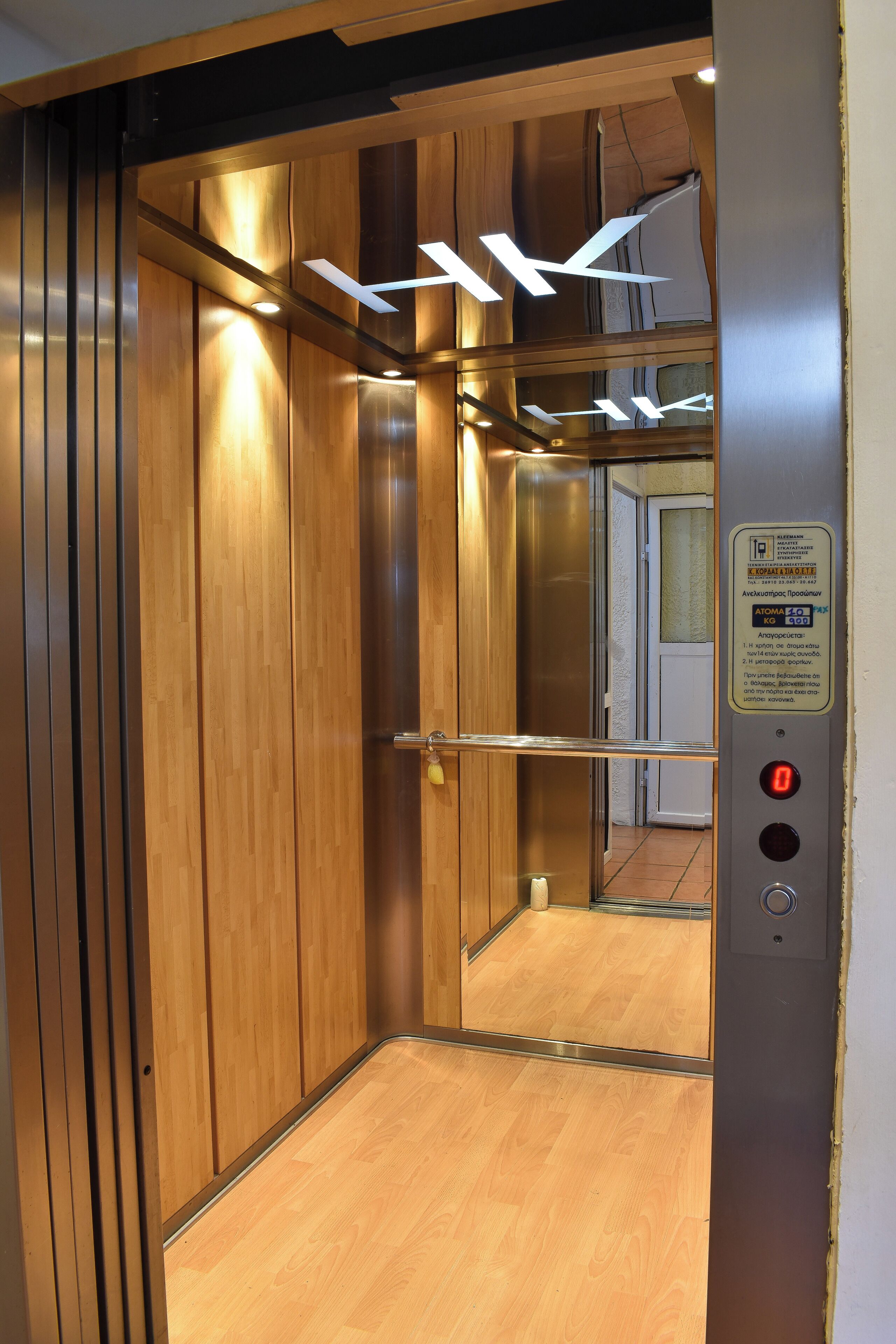 An elevator interior with wooden paneling, a metallic handrail, and a control panel with a red button.