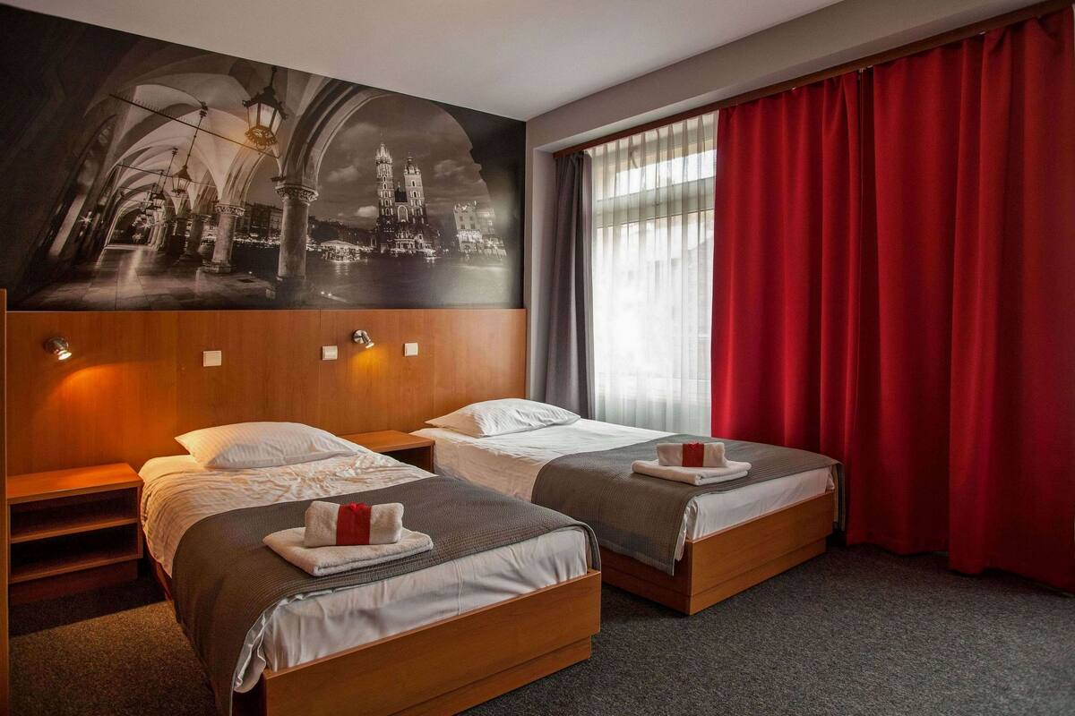 Habitación de hotel con dos camas, un mural grande en la pared y una ventana con cortinas rojas.