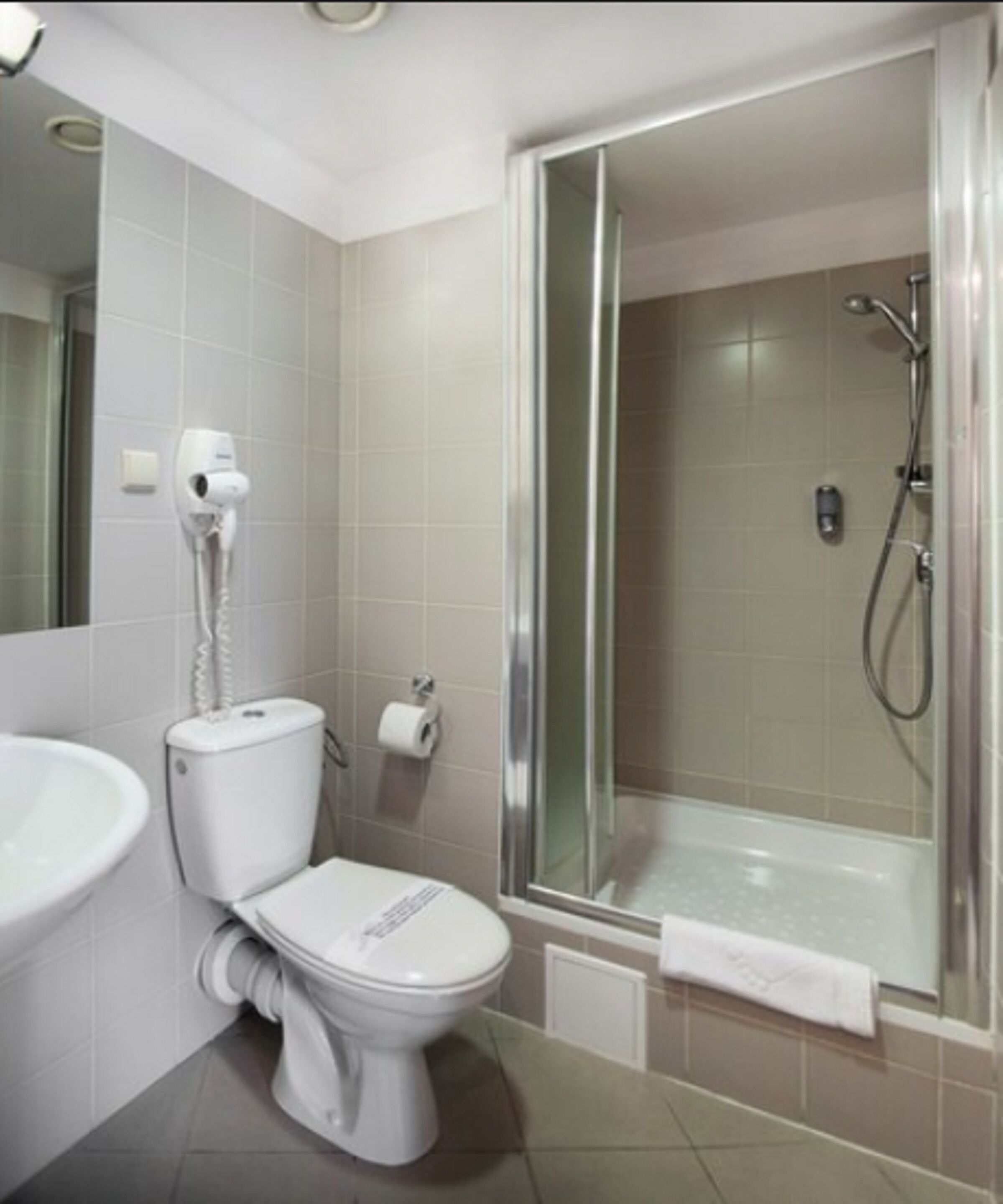 Un baño con inodoro, lavabo, ducha y cabina de ducha con mampara de vidrio.