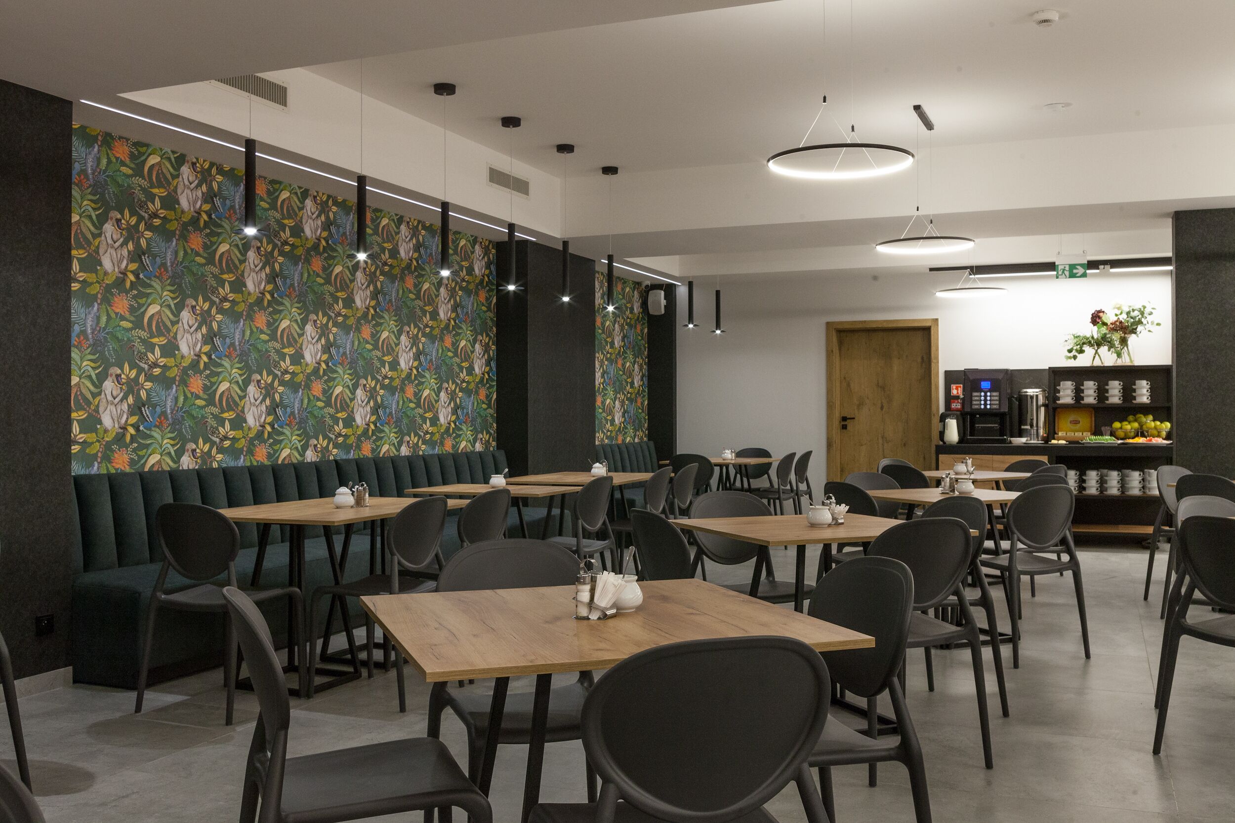A modern restaurant with booths and tables, a patterned wall, and a kitchen area in the background.