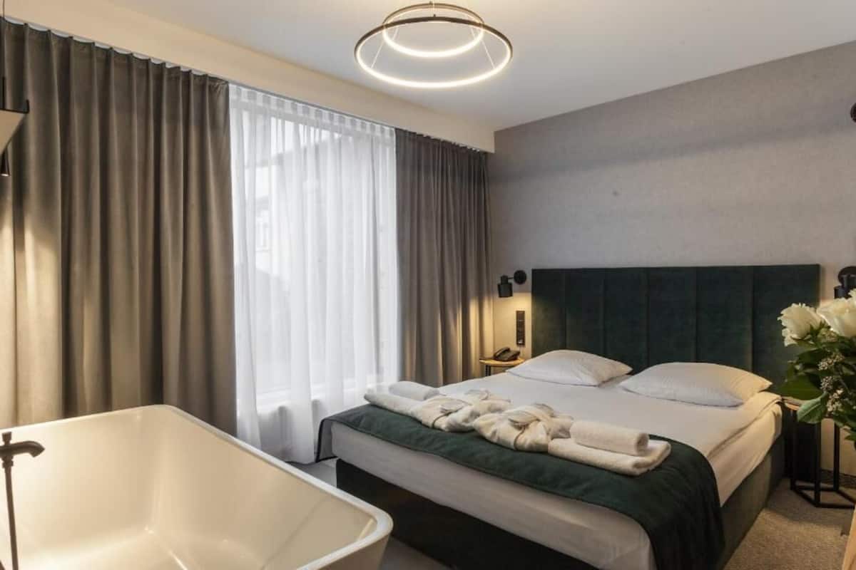 Una habitación de hotel moderna con una cama grande, una bañera y una mesita de noche con lámpara.