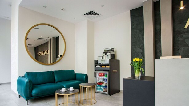 A reception area with a teal sofa, two gold-rimmed tables, a coffee machine, and a refrigerator.