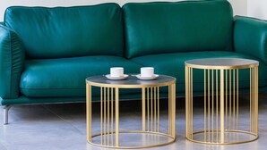 Un canapé de couleur turquoise, deux tables rondes à cadre doré et un grand miroir à cadre doré sur un mur blanc.