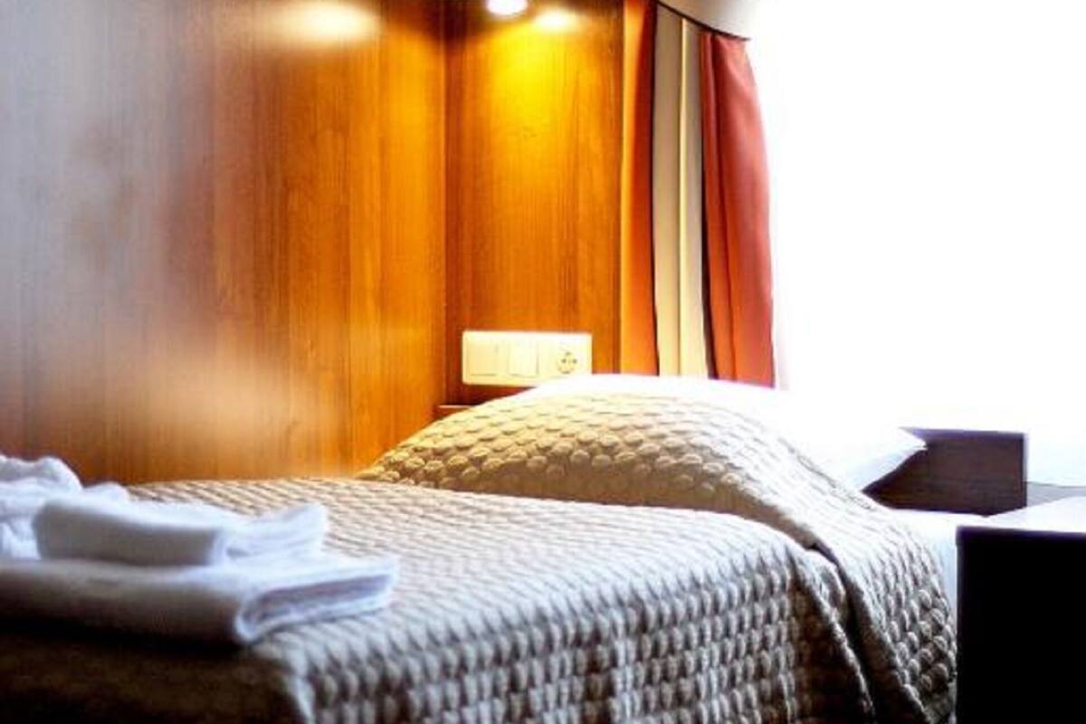 Una habitación de hotel con cabecera de madera, una lámpara de noche, una cama bien hecha con manta y una ventana con cortinas.