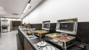 Un buffet avec différents plats présentés dans des récipients en métal, un évier et une plante en arrière-plan.