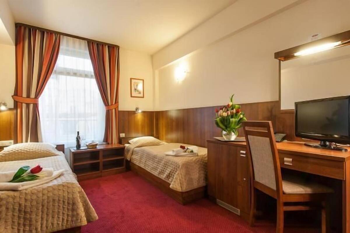 Habitación de hotel con dos camas, un escritorio con televisor, una silla y una mesita con un florero.