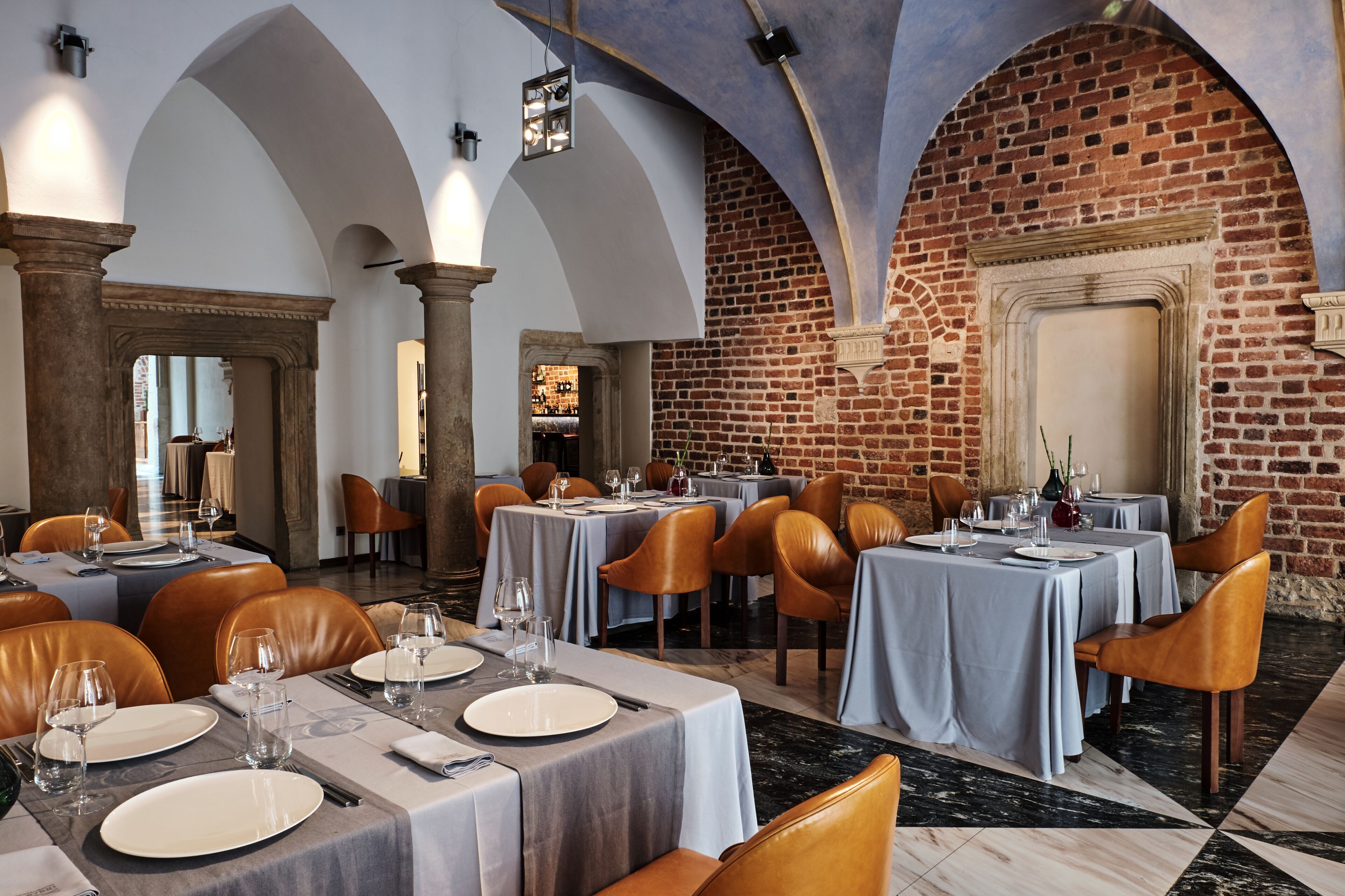 A restaurant with tables set for dining, featuring a brick wall and arched ceilings.
