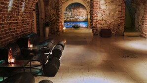 A stone-walled room with a brick fireplace, a stone bench, and a table with chairs. - Hotel Stary (Kraków)