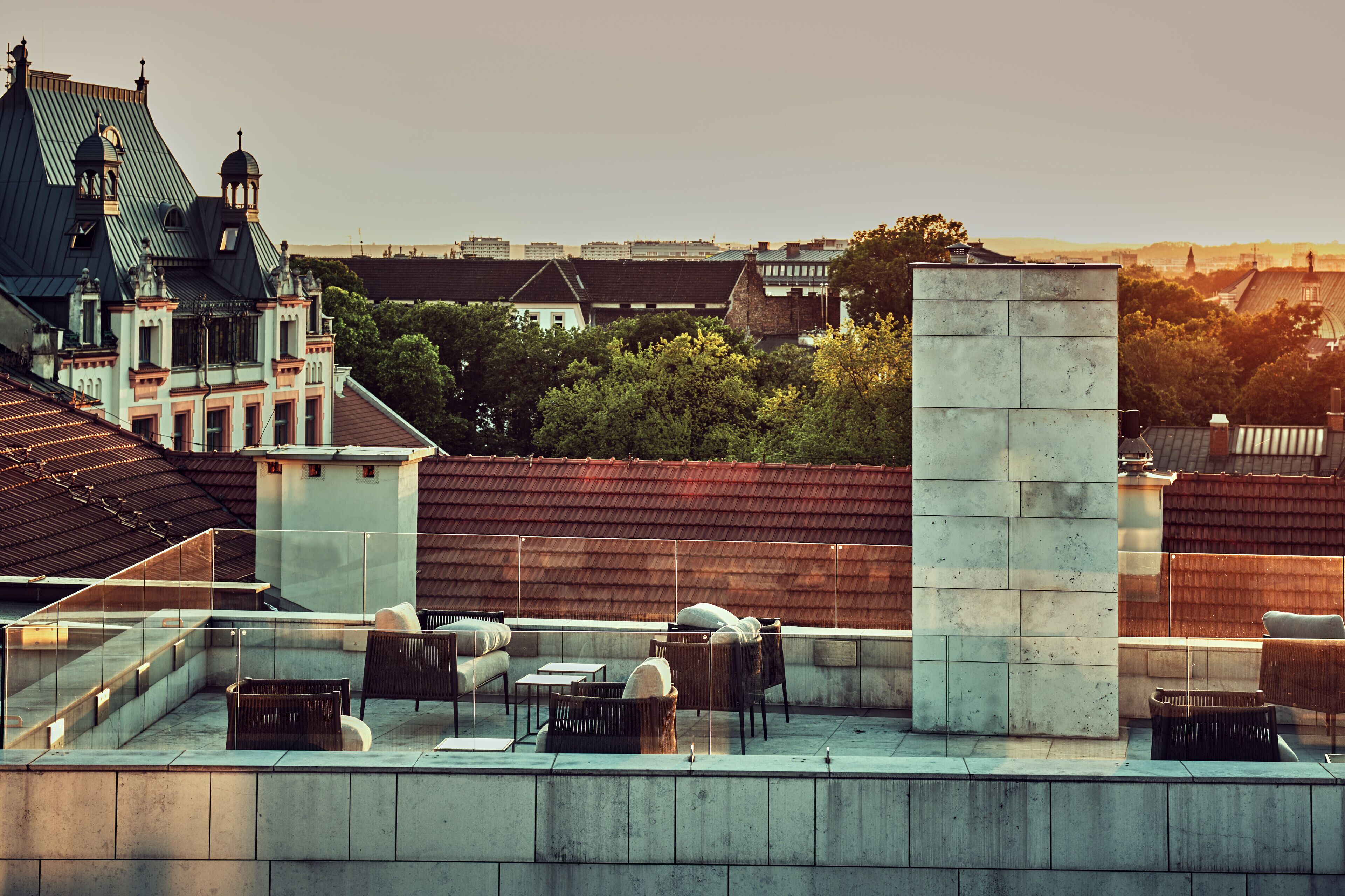 A rooftop terrace with outdoor seating, a stone pillar, and a view of surrounding buildings.