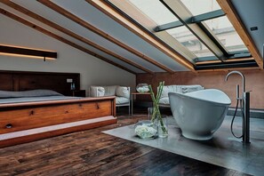 A modern bedroom with a skylight, a large bathtub, and a wooden bed. - Hotel Stary (Kraków)