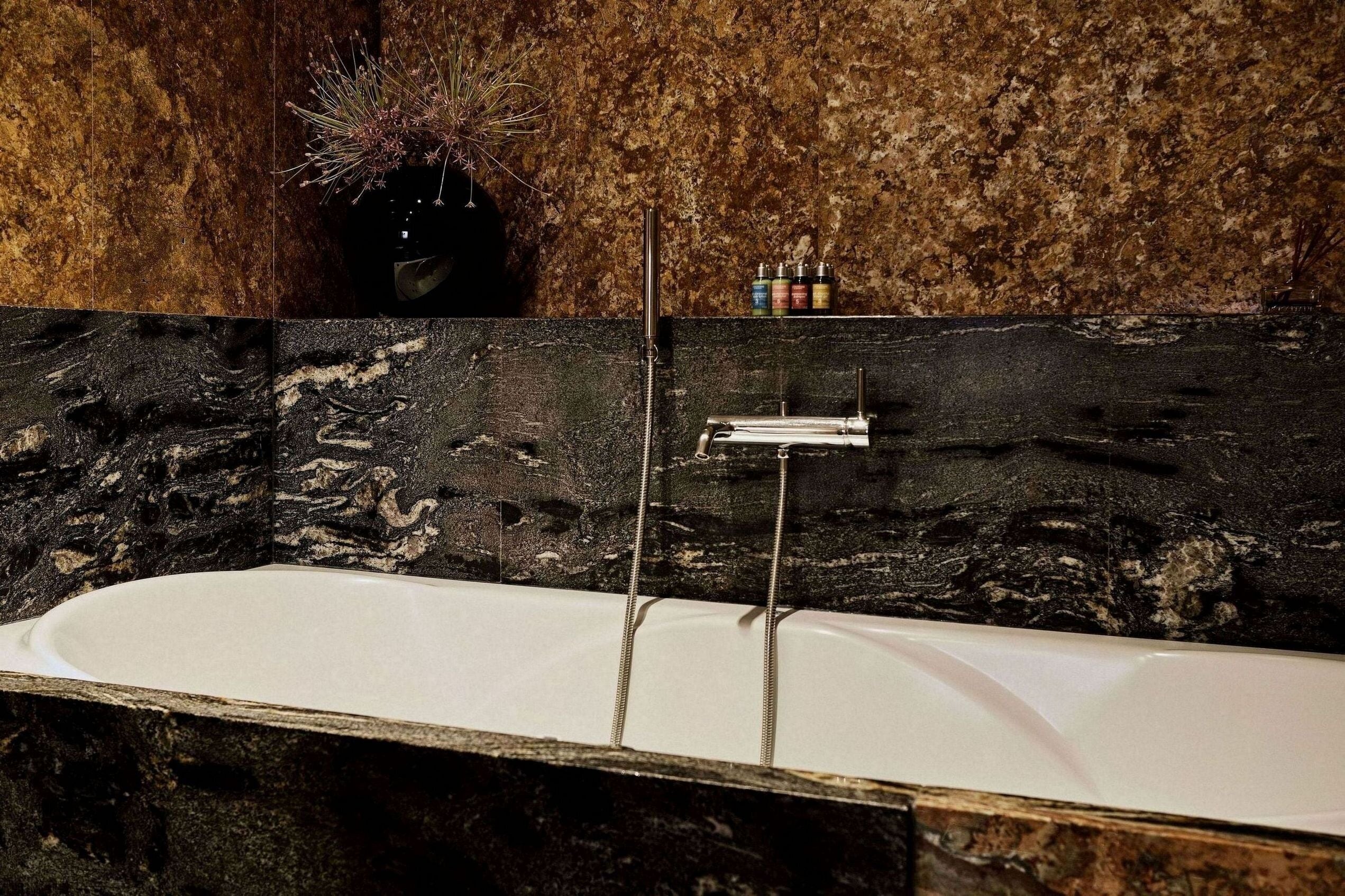 Un baño moderno con lavamanos de mármol, una bañera grande y un estante en la pared con artículos de aseo.