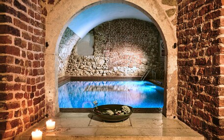 An indoor pool with a stone wall backdrop, a candle, and a decorative bowl on the floor.