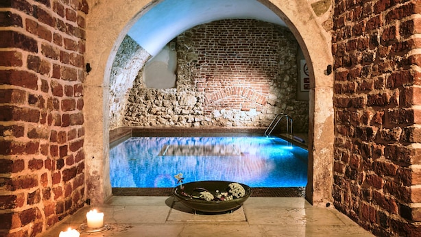 An indoor pool with a stone wall backdrop, a candle, and a decorative bowl on the floor. - Hotel Stary (Kraków)