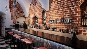 A bar with a brick wall, wooden stools, and shelves of bottles. - Hotel Stary (Kraków)