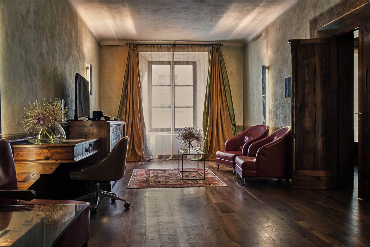 A room with a wooden desk, a chair, a sofa, and a large window with curtains.