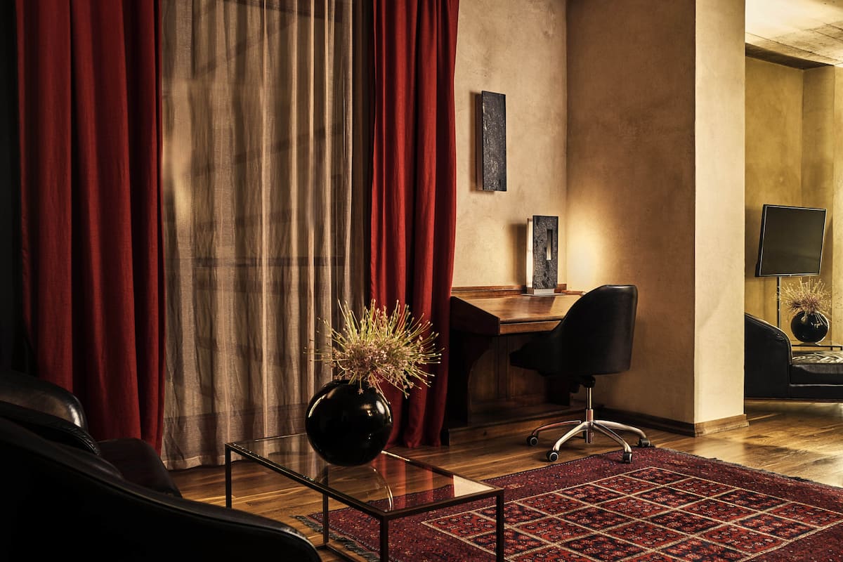 A modern room with a glass coffee table, a black office chair, a desk, and a red curtain.