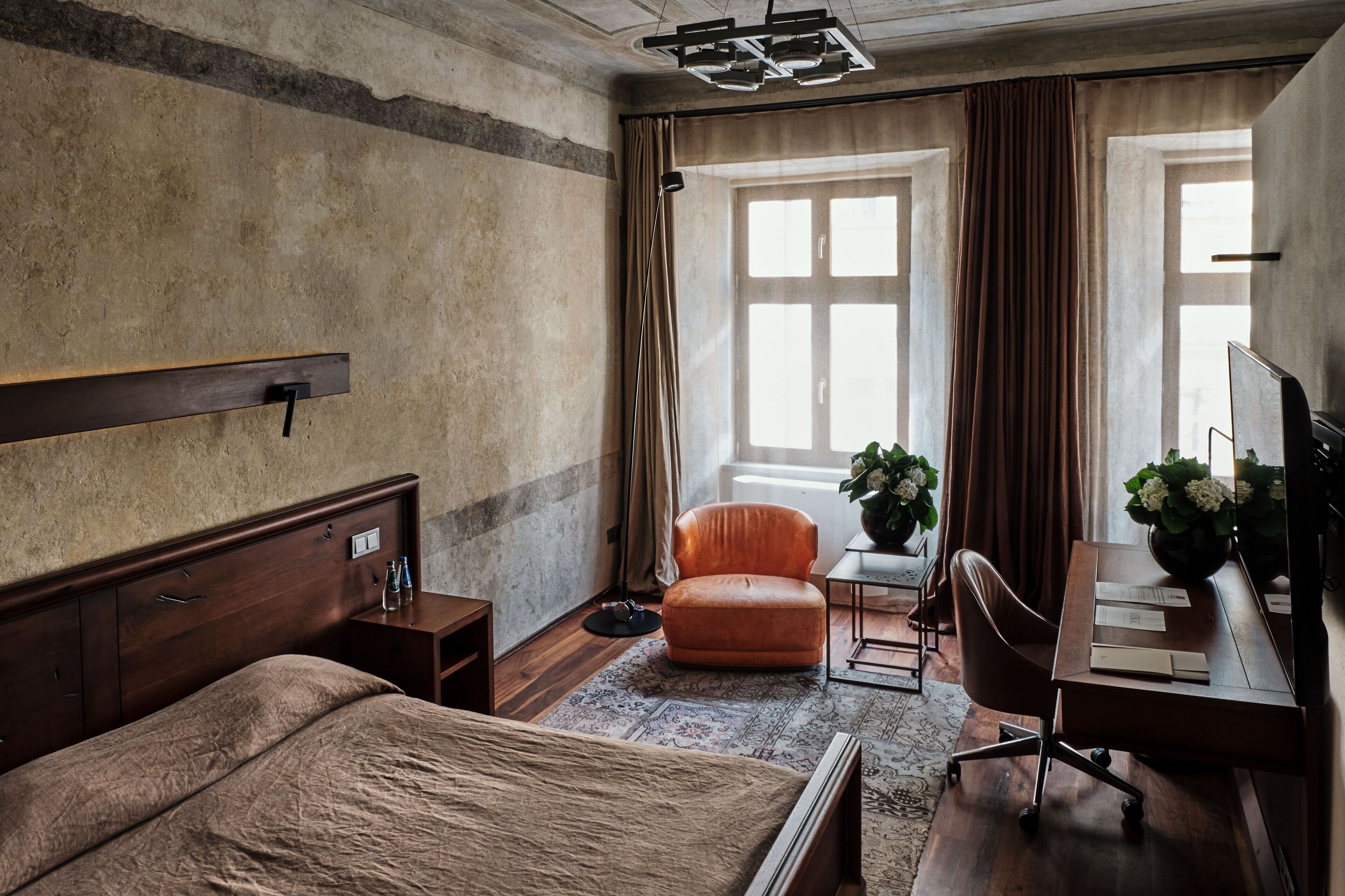 Habitación de hotel con una cama grande, un escritorio con silla, una mesita con una planta y una ventana con cortinas.