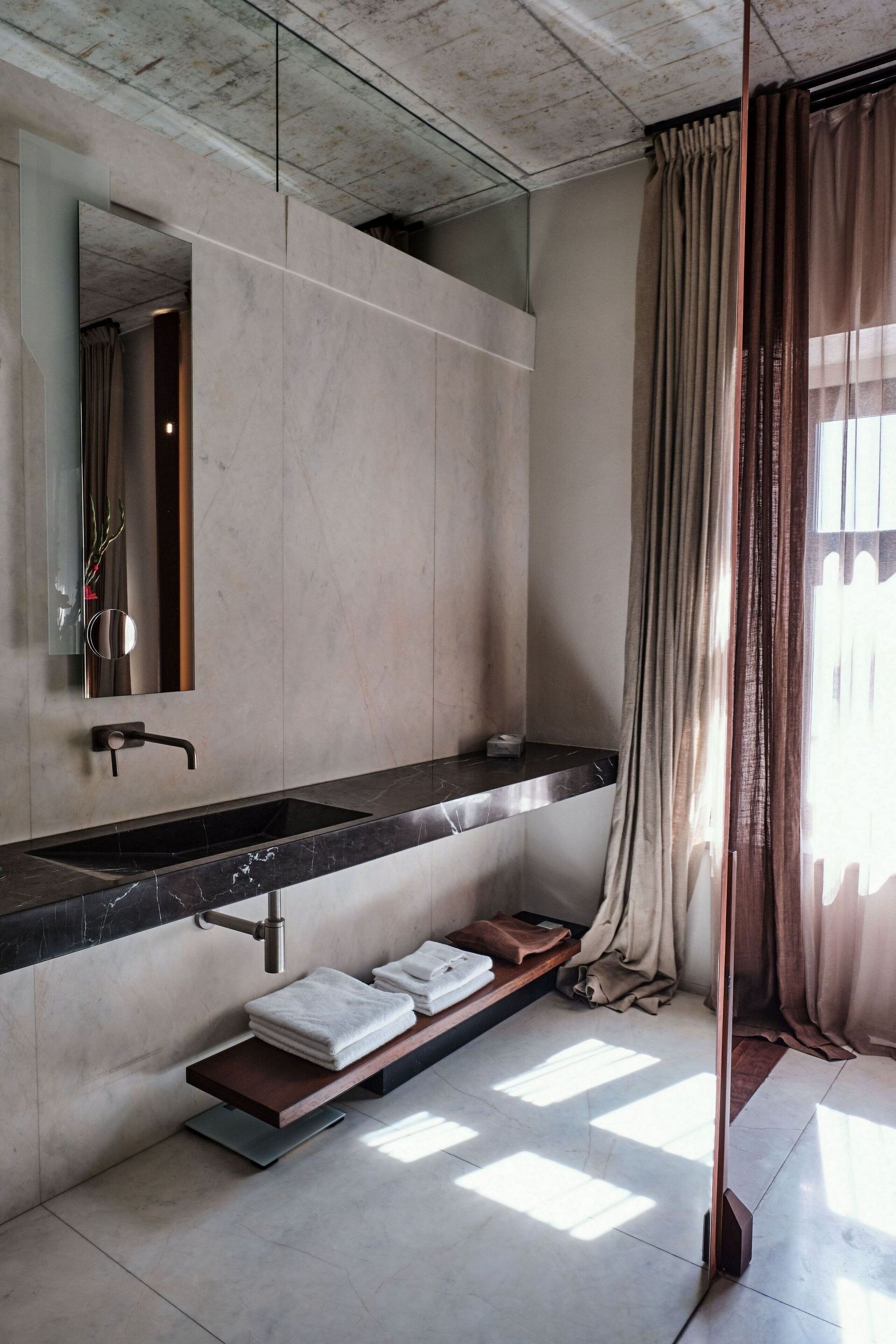 Une salle de bain moderne avec un grand miroir, un lavabo en marbre noir et un porte-serviettes.