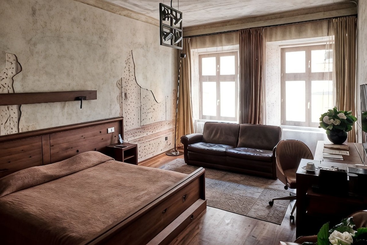 A bedroom with a bed, a desk, a chair, a sofa, and a window with curtains.