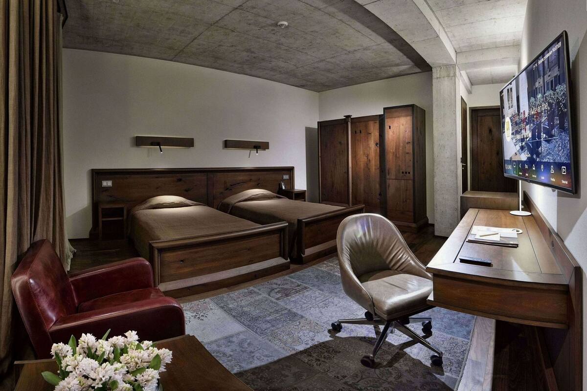 A hotel room with two beds, a desk, a chair, a wardrobe, and a television.