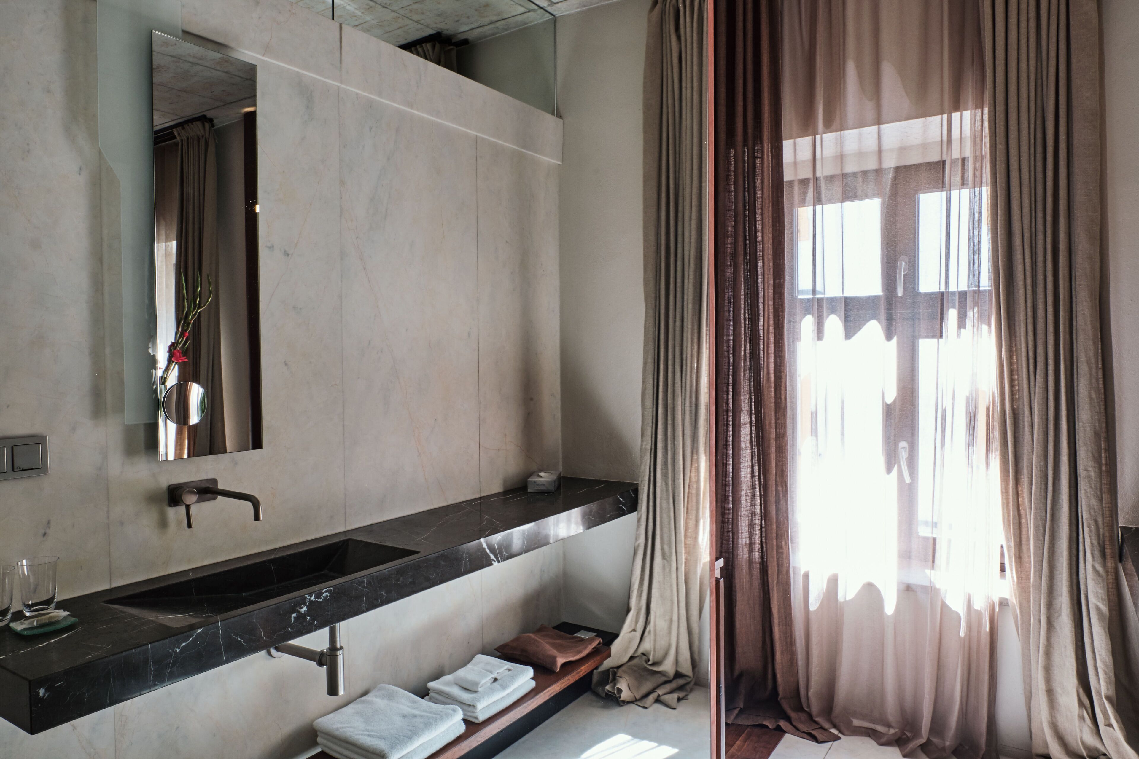 A bathroom with a black marble sink, a mirror, and a window with curtains.