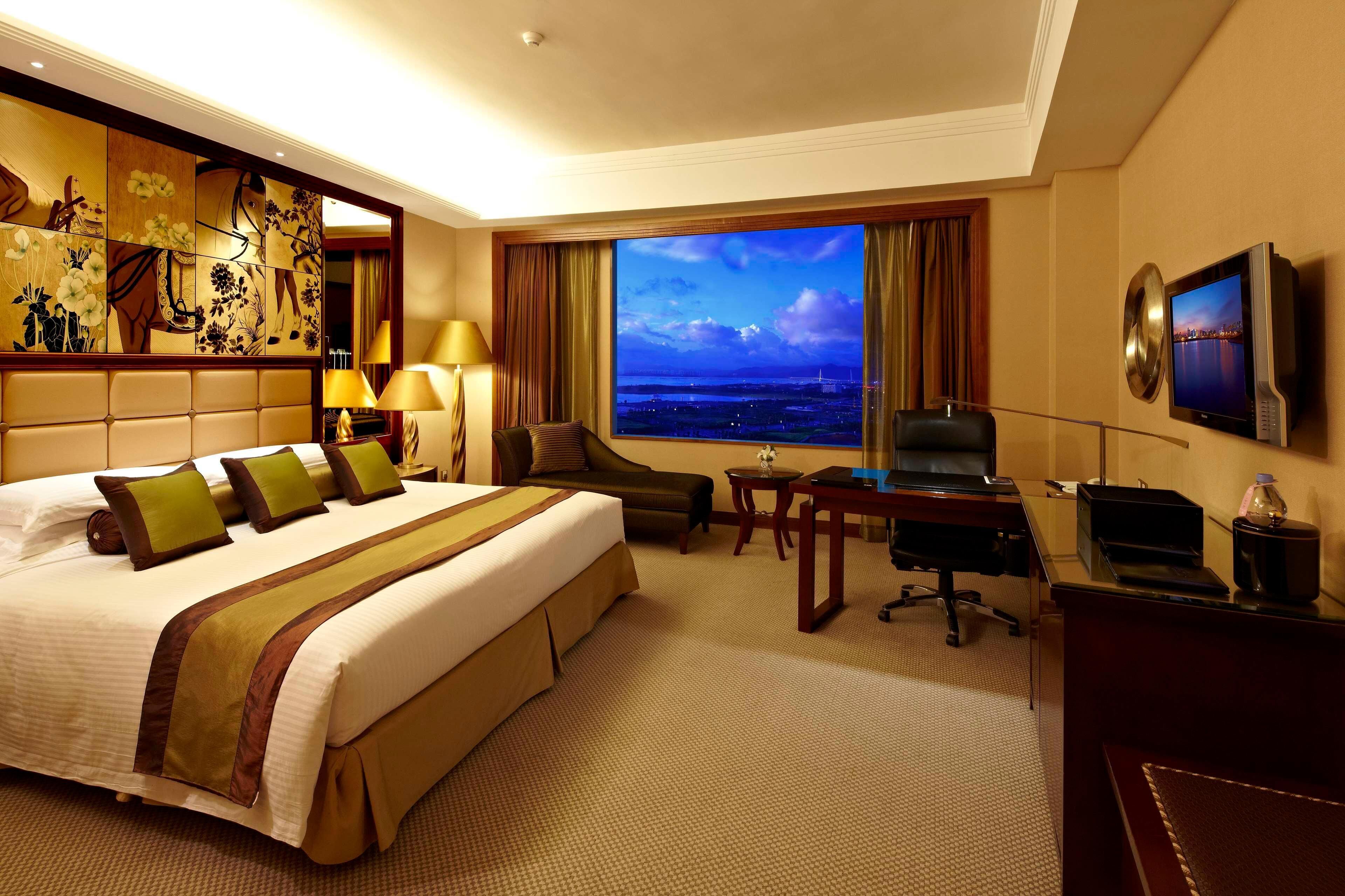 Une chambre d’hôtel avec un grand lit, un bureau, une chaise, une télévision et une vue sur le paysage urbain.