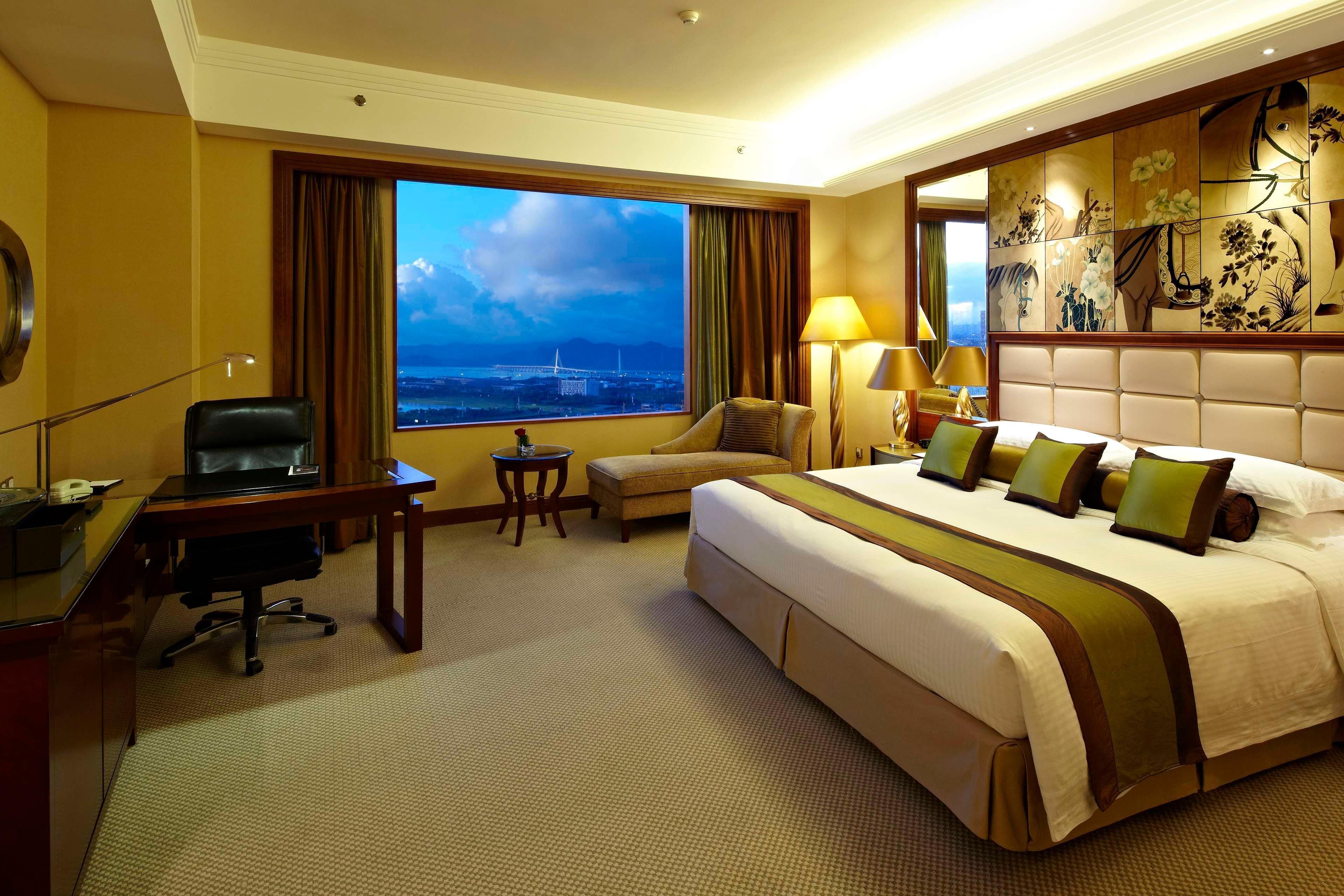 Une chambre d’hôtel avec un grand lit, un bureau, une chaise, une petite table et une vue sur le paysage urbain.