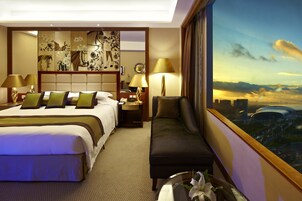 A hotel room with a large bed, a seating area, a nightstand, a lamp, and a view of a cityscape.