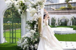 A wedding venue with a green gate, white floral decorations, and a white dress.