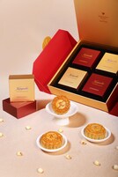 Una colección de pasteles de luna en una caja con interior rojo y exterior dorado, acompañados de un plato pequeño blanco y migas de pastel de luna esparcidas.