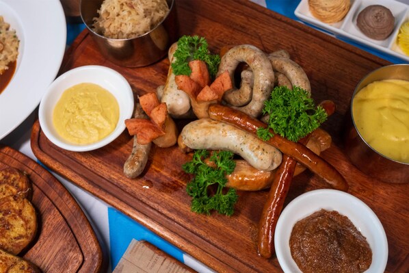 Ein Holzbrett mit verschiedenen Wurstsorten, garniert mit Petersilie, und dazu kleine Schalen mit Beilagen.