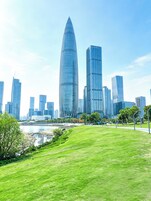 A cityscape with modern skyscrapers, a river, and a grassy park area.