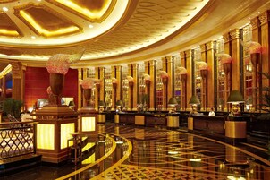 A luxurious lobby with a polished floor, ornate columns, and a reception desk.