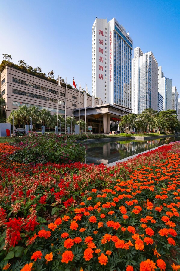 Ein Hotel mit moderner Fassade, großzügigem Eingangsbereich und einem Garten mit roten Blüten.
