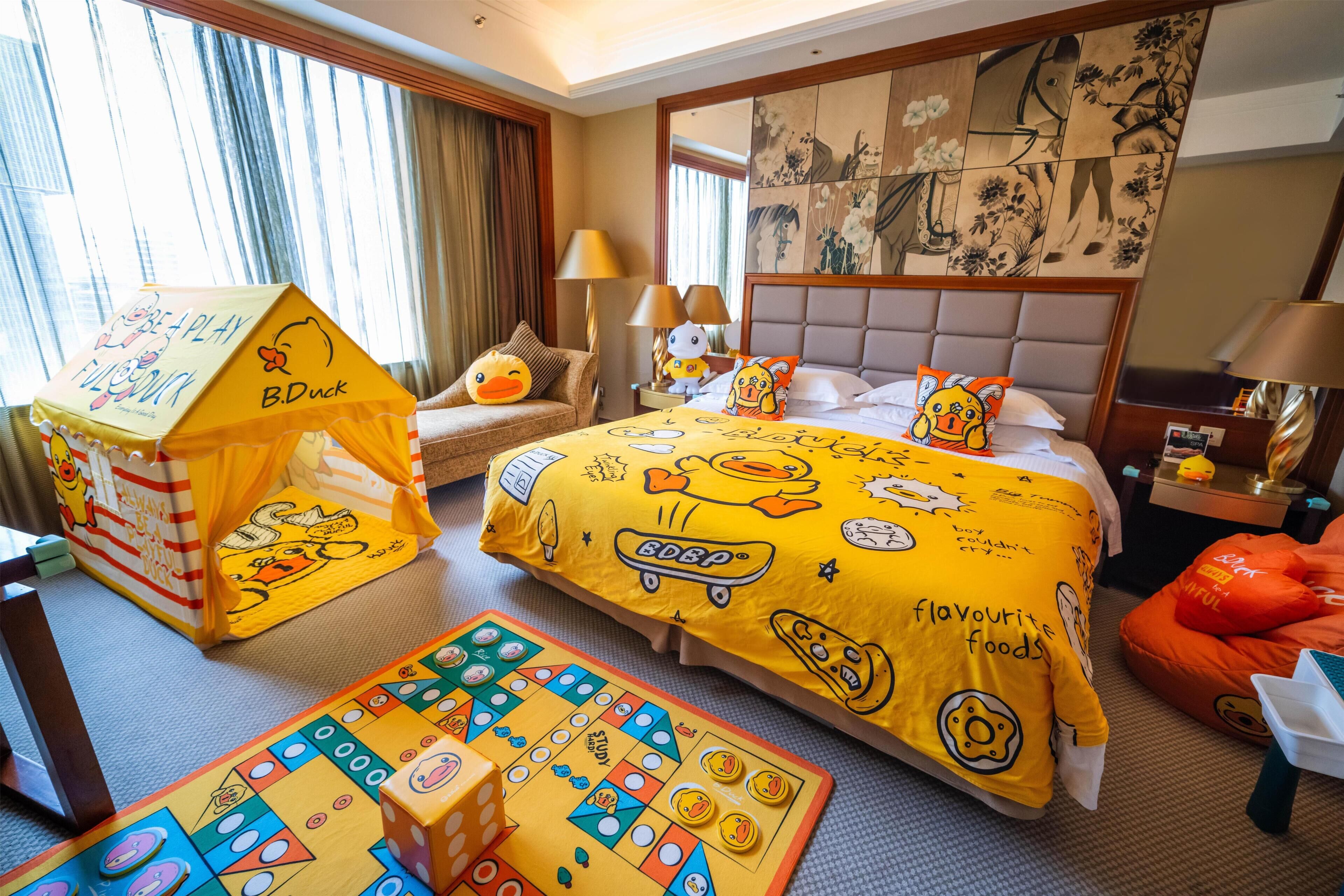 A hotel room with a bed, a playhouse, a board game, and a pillow with duck designs.