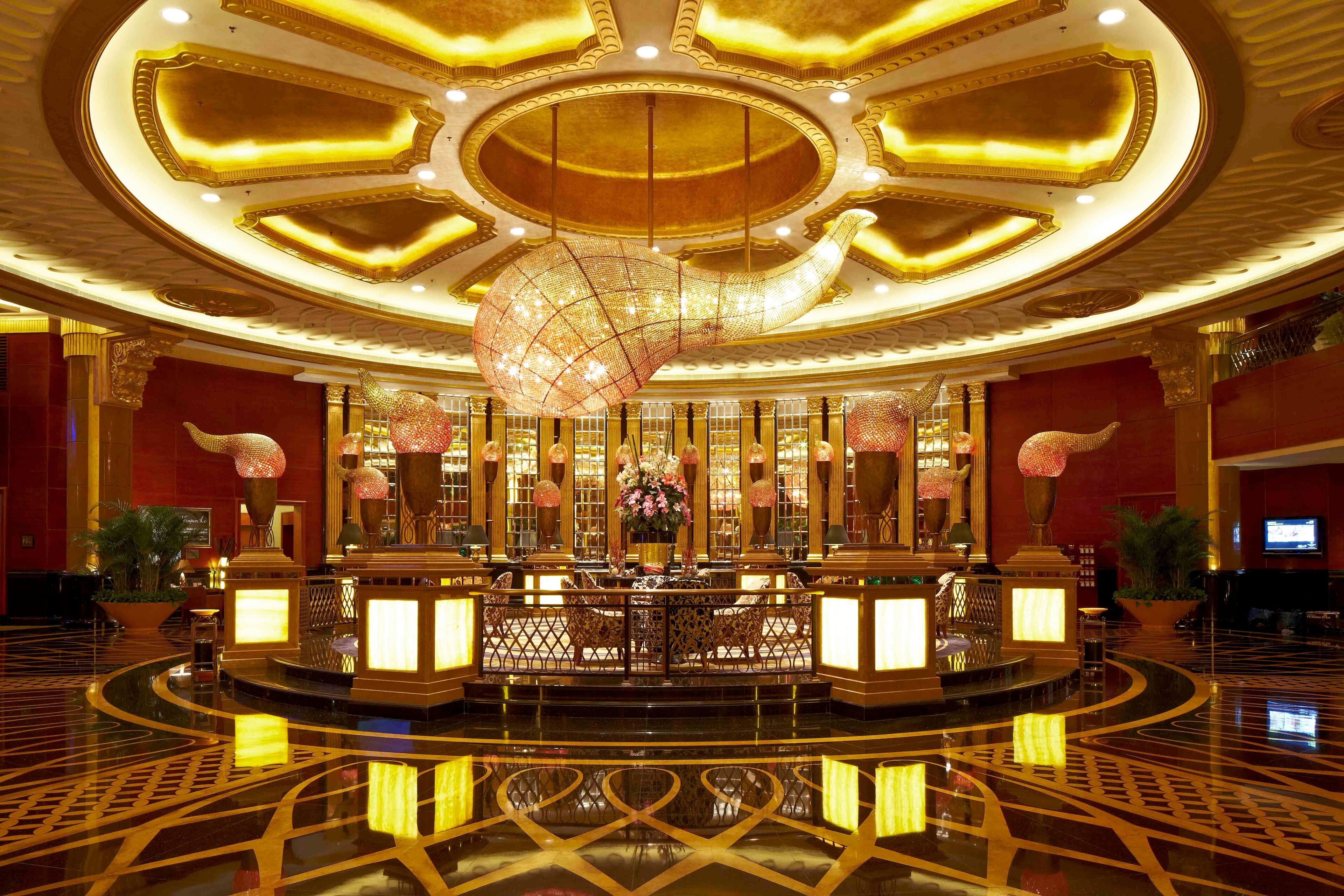 A luxurious lobby with a grand chandelier, ornate columns, and a reflective floor.