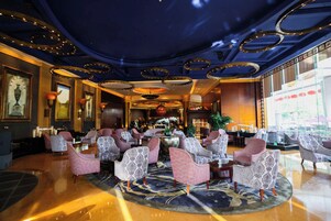 A spacious lobby with a high ceiling, ornate chandeliers, and a large seating area with patterned chairs.