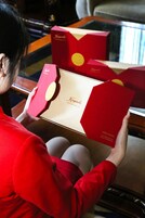 A person holding a red box with a logo, seated at a table with a reflective surface.