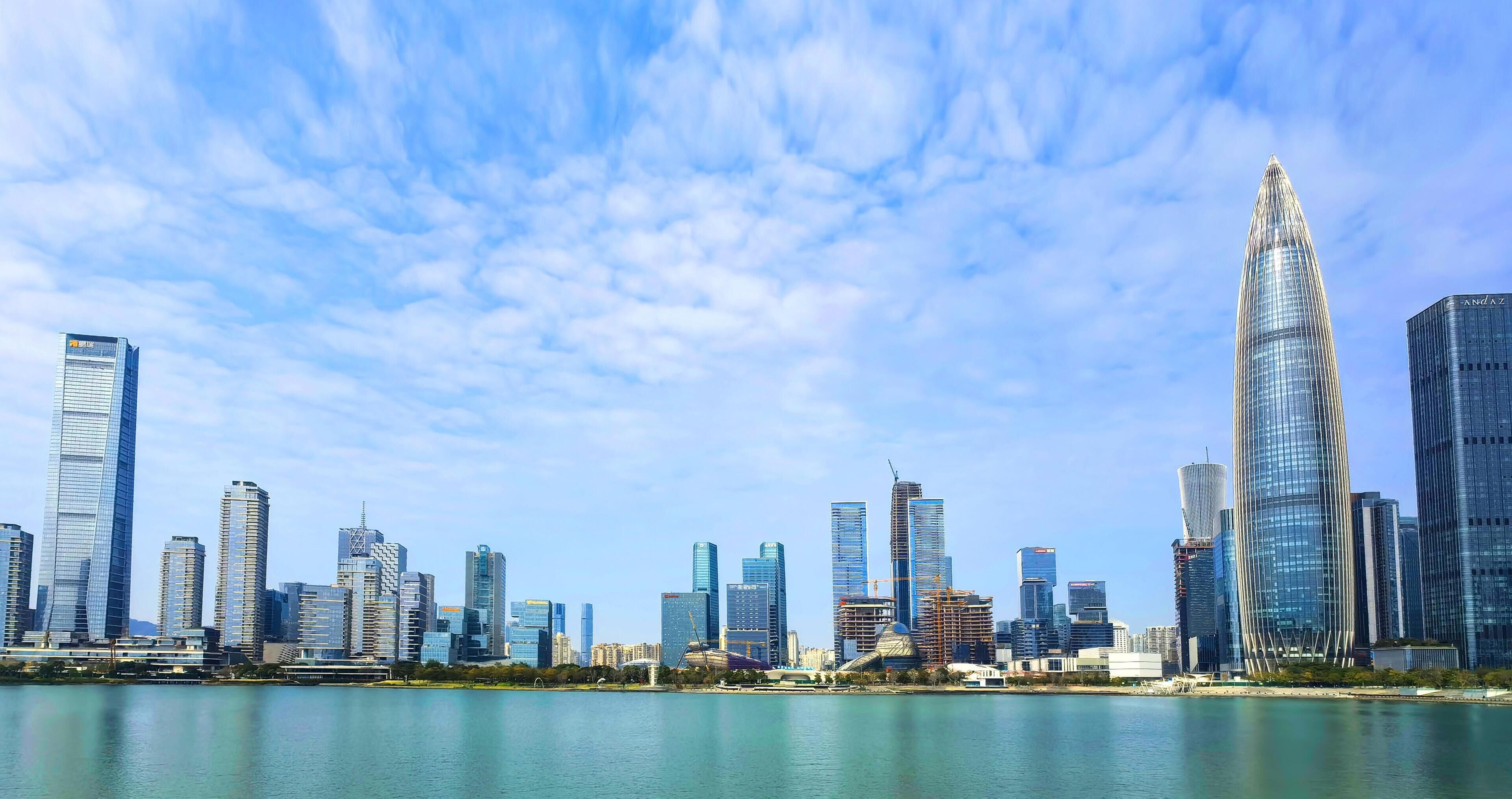 A city skyline with modern skyscrapers, a body of water in the foreground, and a clear sky.
