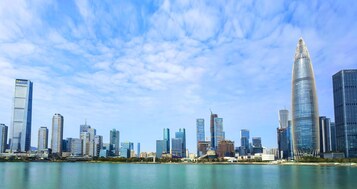 A city skyline with modern skyscrapers, a body of water in the foreground, and a clear sky.