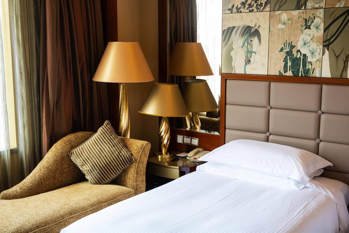 A hotel room with a bed, a chair, and two lamps.