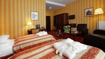 Habitación de hotel con paredes a rayas amarillas y anaranjadas, dos camas con cubrecamas estampados, un escritorio con una computadora portátil, una silla, un televisor y una lámpara.