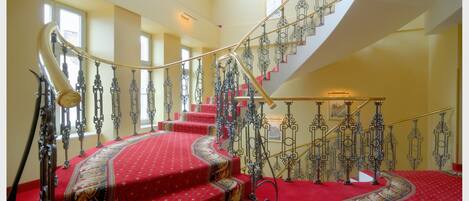 A grand staircase with ornate metal railings and red carpeted steps.