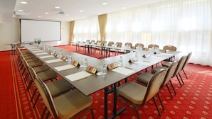 A conference room with a long table, chairs, nameplates, water bottles, and a projector screen.