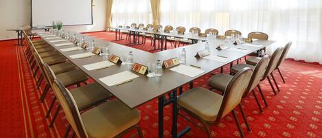 A conference room with a long table, chairs, nameplates, water bottles, and a projector screen.