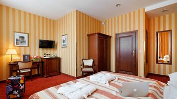 A hotel room with a bed, a desk with a computer, a TV, a wardrobe, and a suitcase.