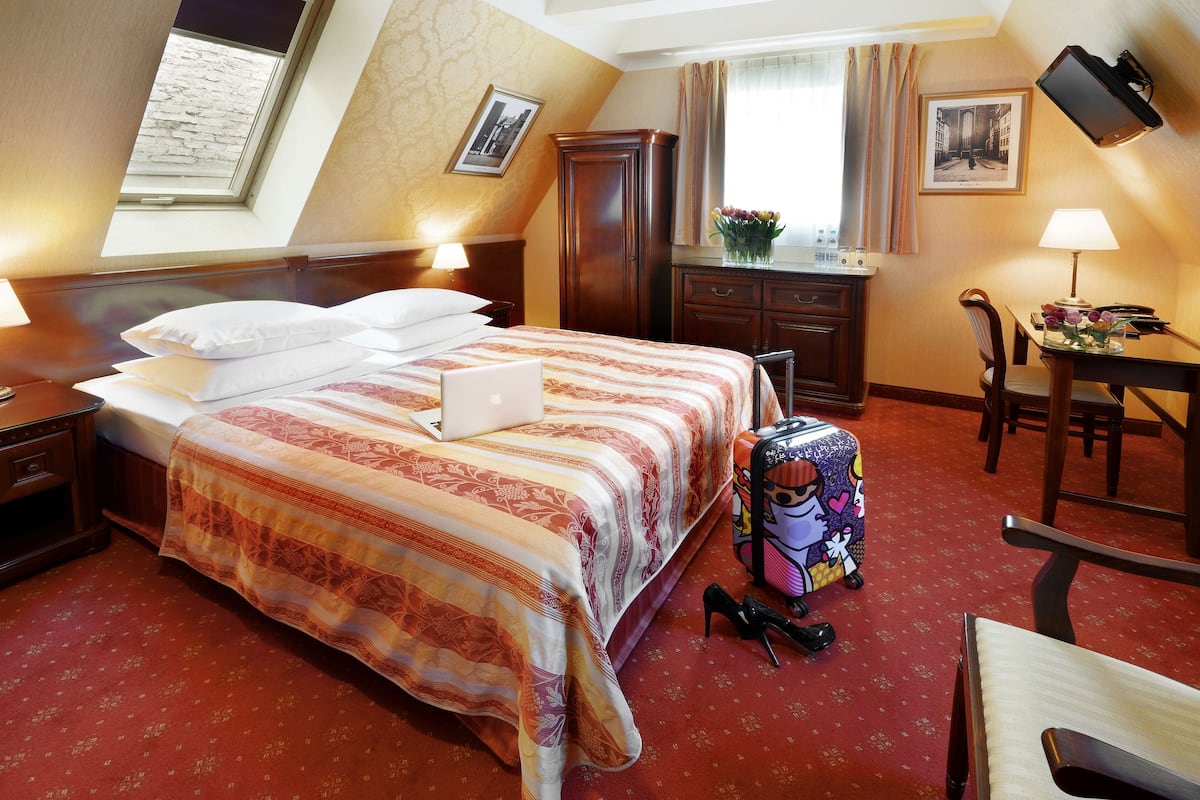 A hotel room with a bed, a desk, a chair, a suitcase, and a window with curtains.