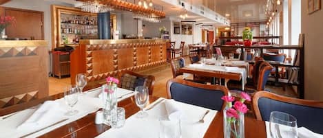 Un restaurante con zona de bar, mesas dispuestas con manteles blancos y sillas.